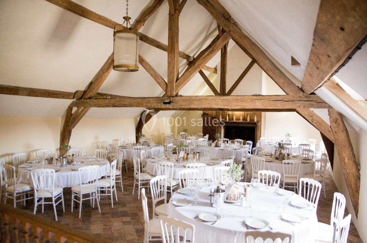 Location salle Wy-dit-Joli-Village (Val-d'Oise) - Château d'Hazeville #11 Salle de réception lumineuse avec poutres apparentes, tables rondes dressées et chaises blanches alignées.