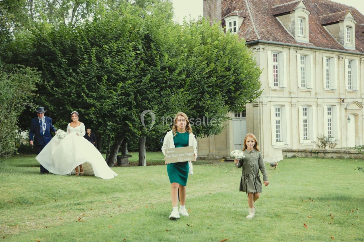 Location salle Wy-dit-Joli-Village (Val-d'Oise) - Château d'Hazeville #28 Deux enfants marchent sur une pelouse devant une mariée et un homme, près d'une grande maison ancienne.