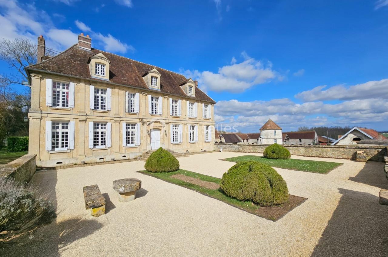 Location salle Wy-dit-Joli-Village (Val-d'Oise) - Château d'Hazeville #8 Façade d'une maison de style classique avec jardin aménagé, ciel bleu et quelques nuages en arrière-plan.