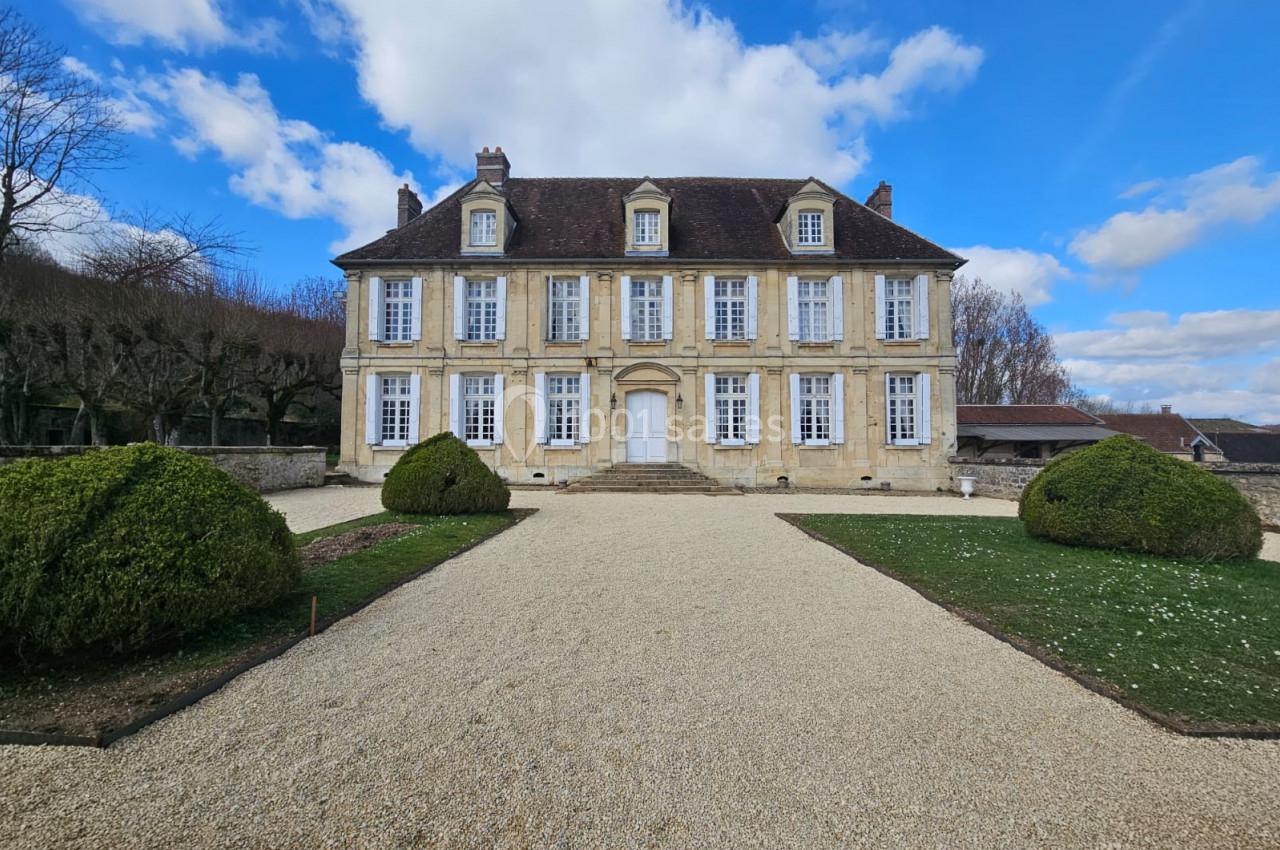 Location salle Wy-dit-Joli-Village (Val-d'Oise) - Château d'Hazeville #25 Façade d'un manoir en pierre avec toit en ardoise, entouré d'un jardin et d'une allée gravillonnée sous un ciel bleu.