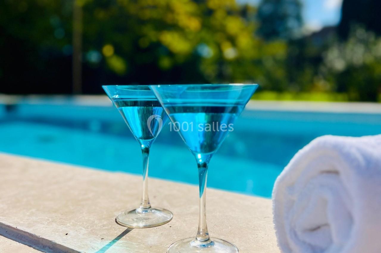 Location salle Wy-dit-Joli-Village (Val-d'Oise) - Château d'Hazeville #37 Deux verres de cocktail bleu posés sur le bord d'une piscine, avec une serviette blanche enroulée à côté.
