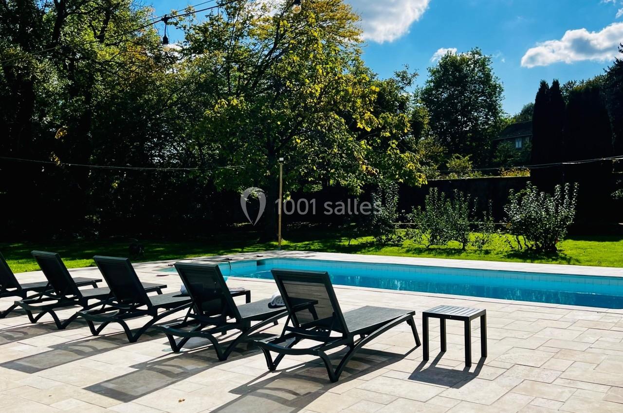 Location salle Wy-dit-Joli-Village (Val-d'Oise) - Château d'Hazeville #5 Chaises longues noires alignées près d'une piscine extérieure entourée de verdure sous un ciel ensoleillé.