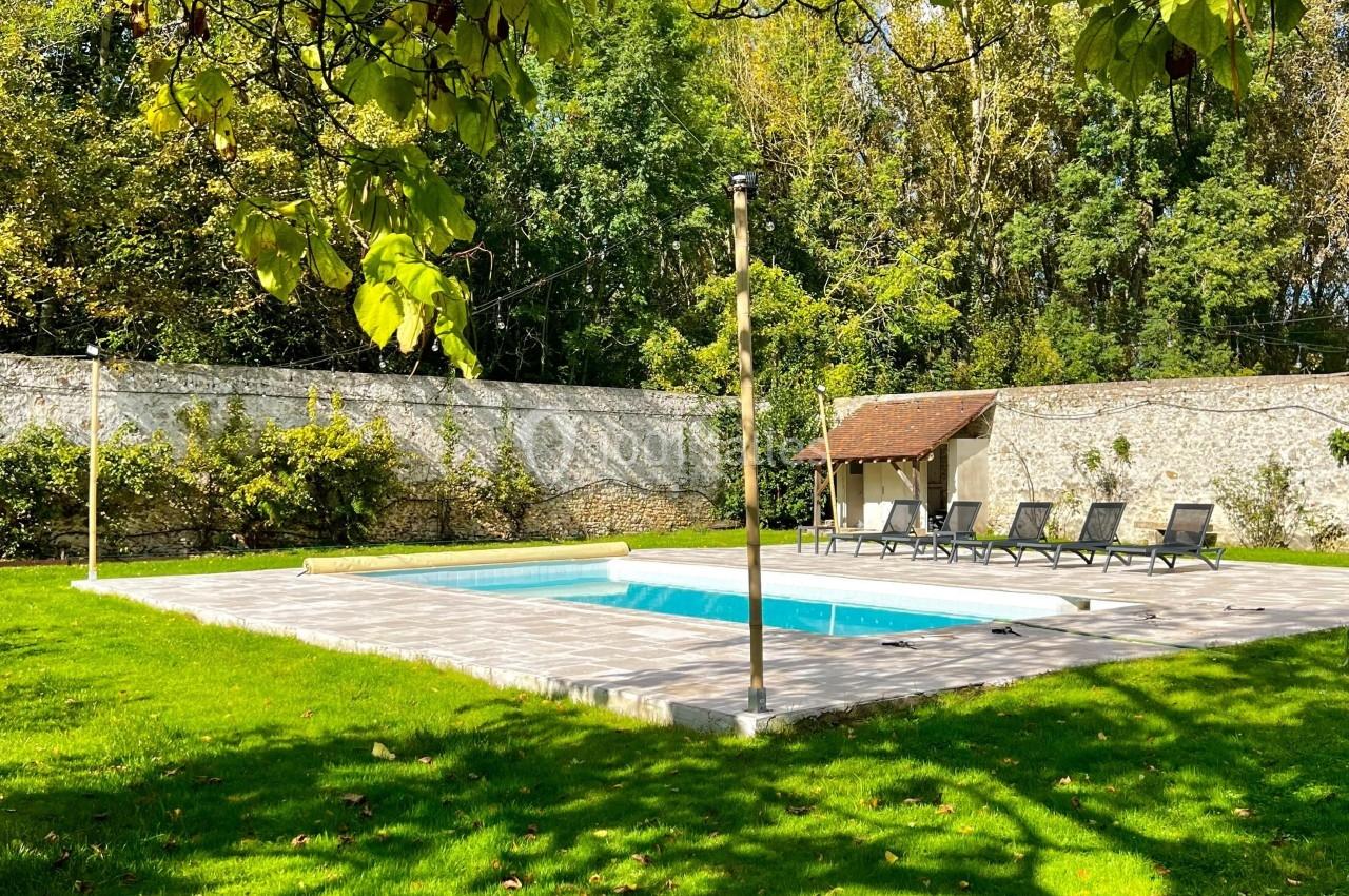 Location salle Wy-dit-Joli-Village (Val-d'Oise) - Château d'Hazeville #4 Piscine extérieure entourée de verdure, avec des transats alignés sur une terrasse en pierre et un mur en arrière-plan.