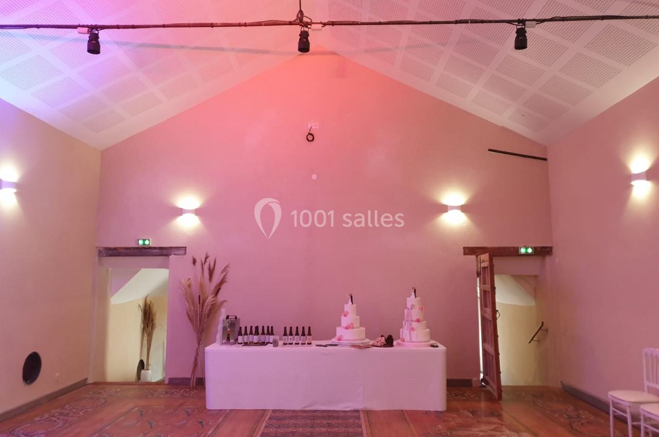 Salle fontaine - 80m² Table décorée avec des bouteilles de vin et un gâteau de mariage à plusieurs étages dans une salle aux murs beige clair.