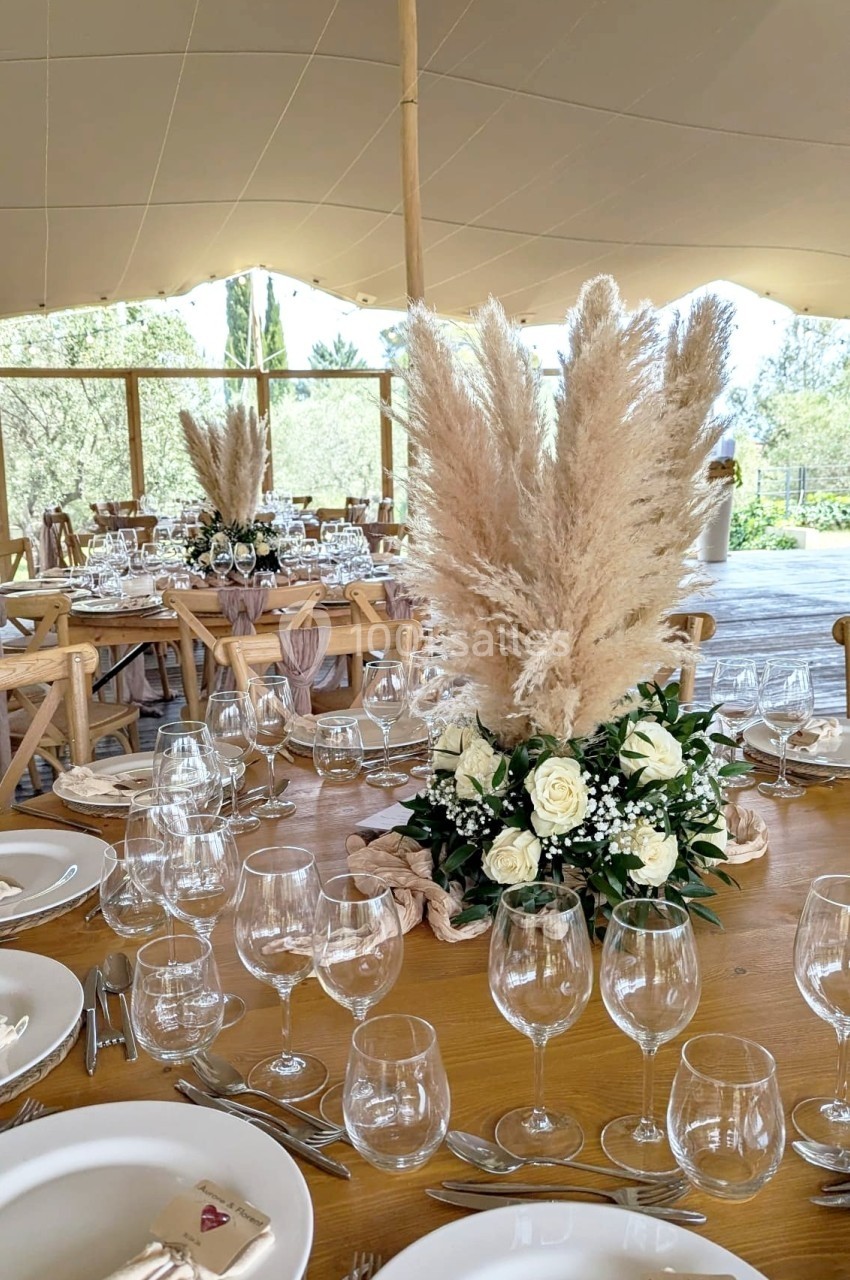 Table de réception décorée avec des roses blanches, des herbes de la pampa et une vaisselle élégante sous une tente ouverte.