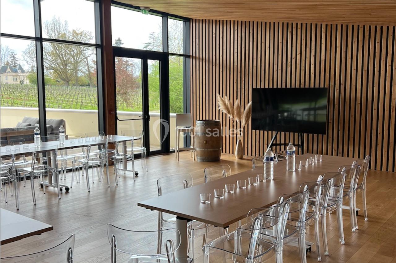 Salle de réunion lumineuse avec tables en bois, chaises transparentes, écran et grandes baies vitrées donnant sur l…