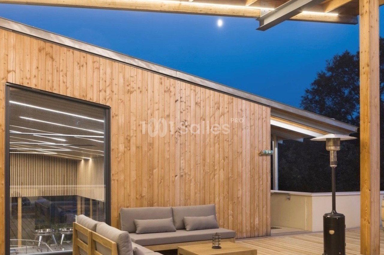Terrasse en bois avec mobilier d'extérieur, éclairage intégré et vue sur un bâtiment moderne en soirée.