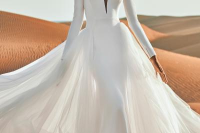 Miniature Via Novias #3 Femme portant une robe de mariée blanche avec un dos ouvert, posant dans un jardin fleuri.