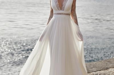 Miniature Via Novias #7 Femme portant une robe de mariée blanche avec un dos ouvert, posant dans un jardin fleuri.