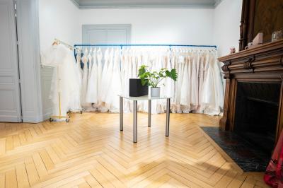 Miniature Via Novias #8 Femme portant une robe de mariée blanche avec un dos ouvert, posant dans un jardin fleuri.