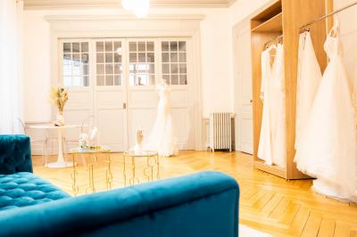 Miniature Via Novias #4 Femme portant une robe de mariée blanche avec un dos ouvert, posant dans un jardin fleuri.