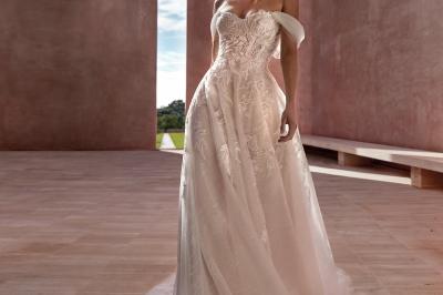 Miniature Via Novias #9 Femme portant une robe de mariée blanche avec un dos ouvert, posant dans un jardin fleuri.