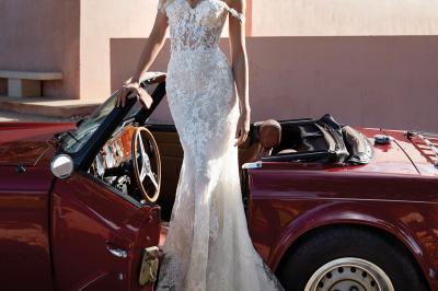 Miniature Via Novias #13 Femme portant une robe de mariée blanche avec un dos ouvert, posant dans un jardin fleuri.