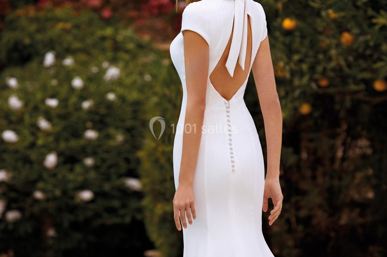 Femme portant une robe de mariée blanche avec un dos ouvert, posant dans un jardin fleuri.