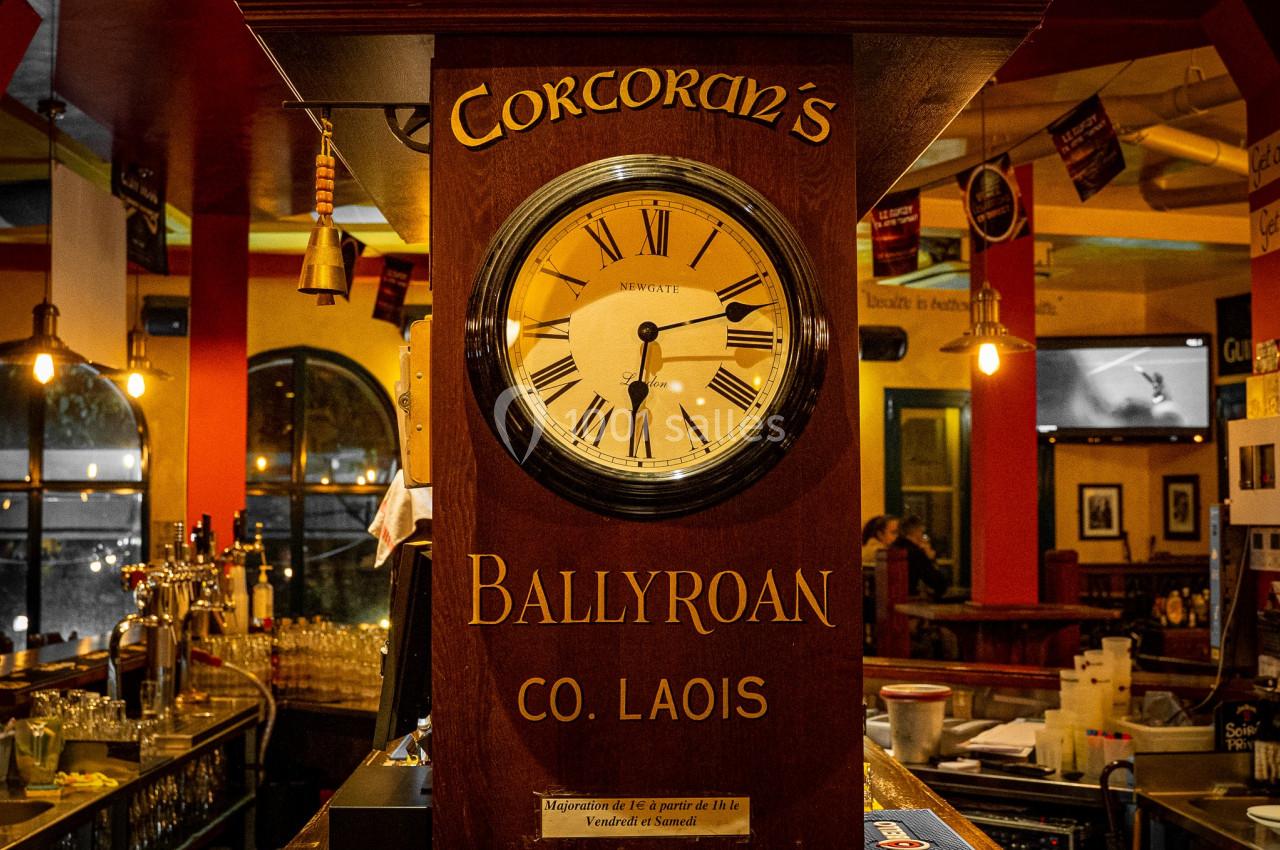 Horloge murale en bois avec inscription ’Corcoran's Ballyroan Co. Laois’, située dans un bar à l'ambiance chaleureuse.