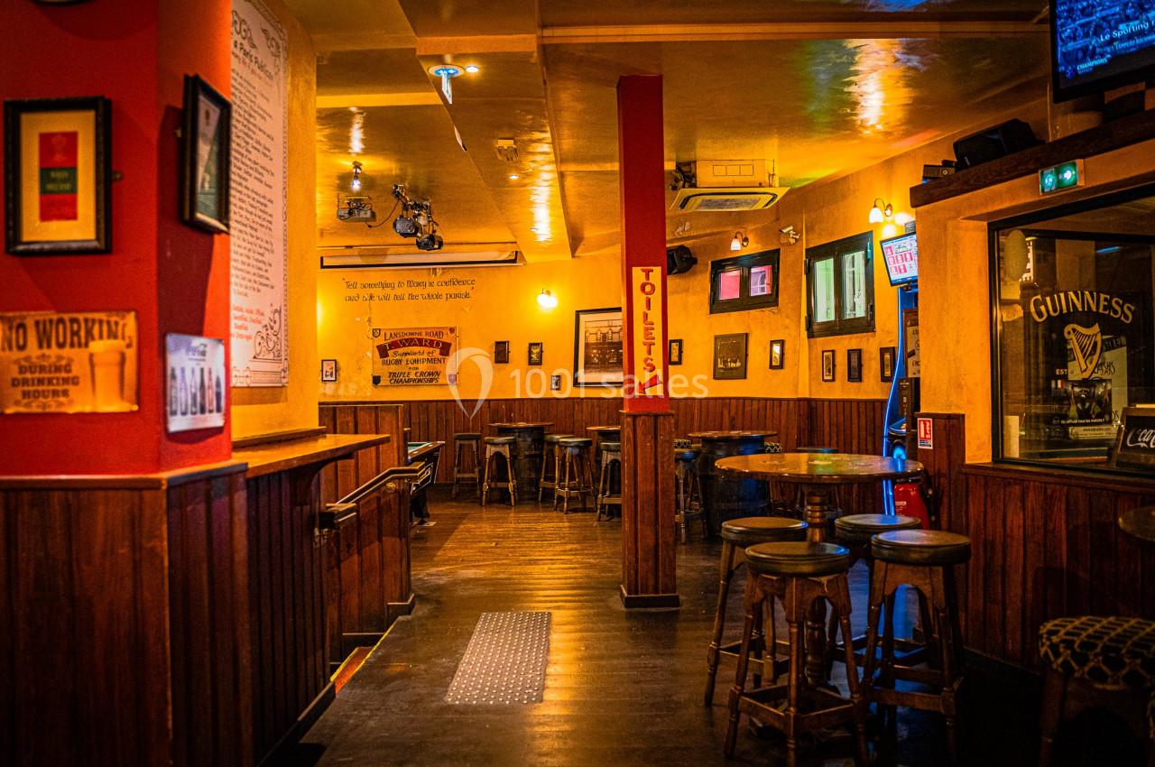 Intérieur d'un pub chaleureux avec des tables en bois, des tabourets hauts et des murs décorés d'affiches.