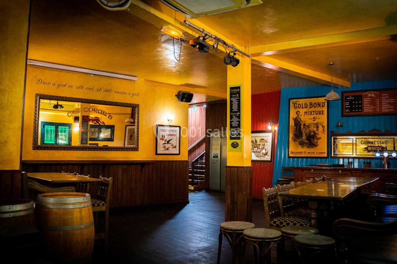Intérieur d'un pub chaleureux avec des murs colorés, des tables en bois et des affiches décoratives vintage.