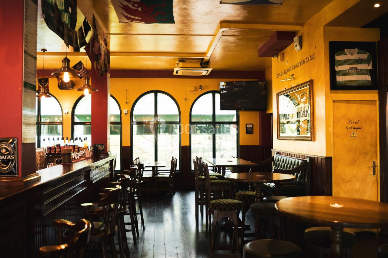 Intérieur d'un pub chaleureux avec bar en bois, tables, chaises, fenêtres cintrées et éclairage tamisé.