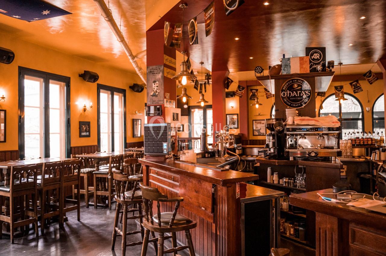 Intérieur d'un pub chaleureux avec un bar en bois, des tables hautes et une décoration conviviale.