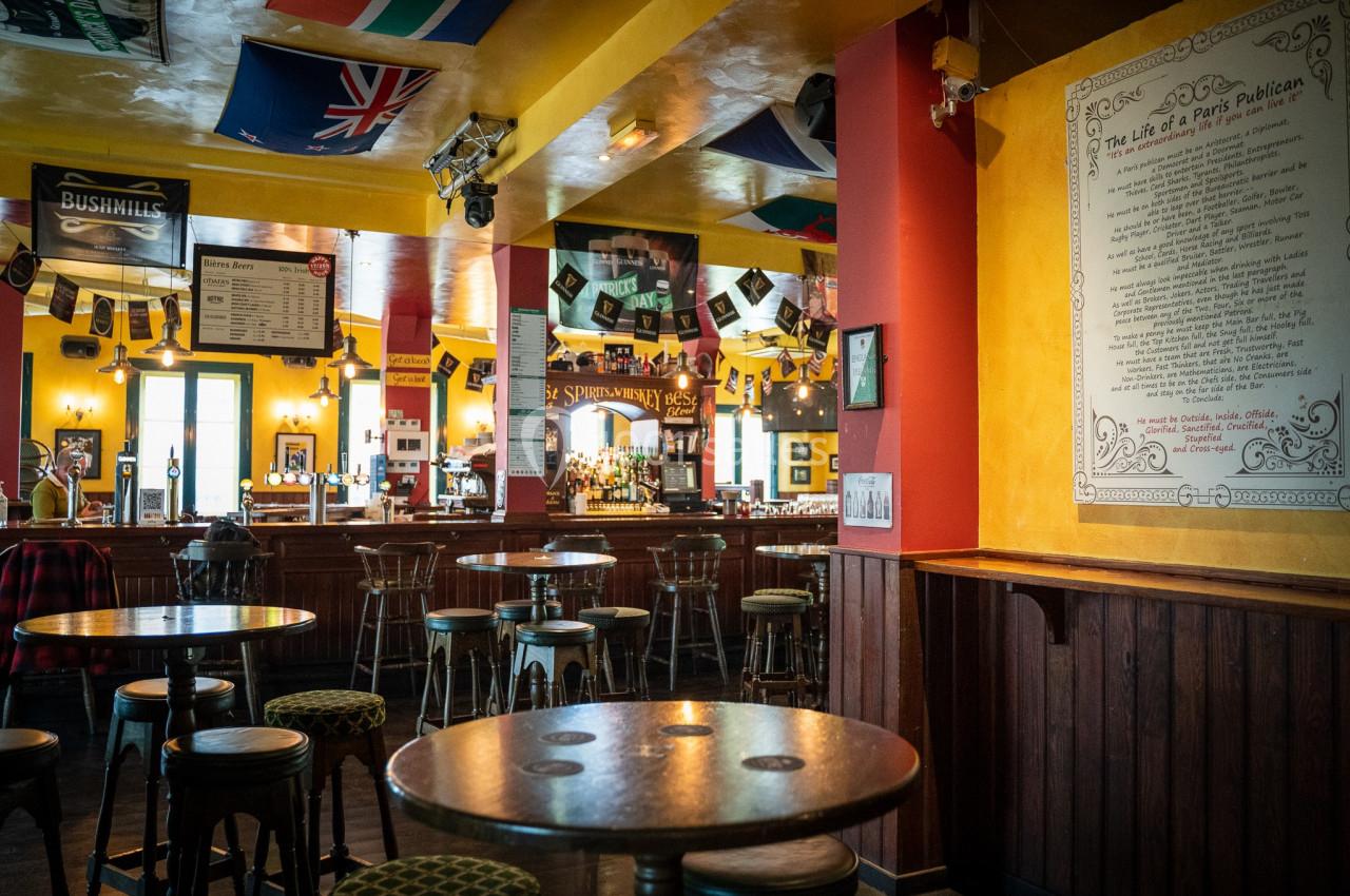 Intérieur d'un pub chaleureux avec des tables, des chaises hautes, des drapeaux suspendus et un menu affiché au mur.