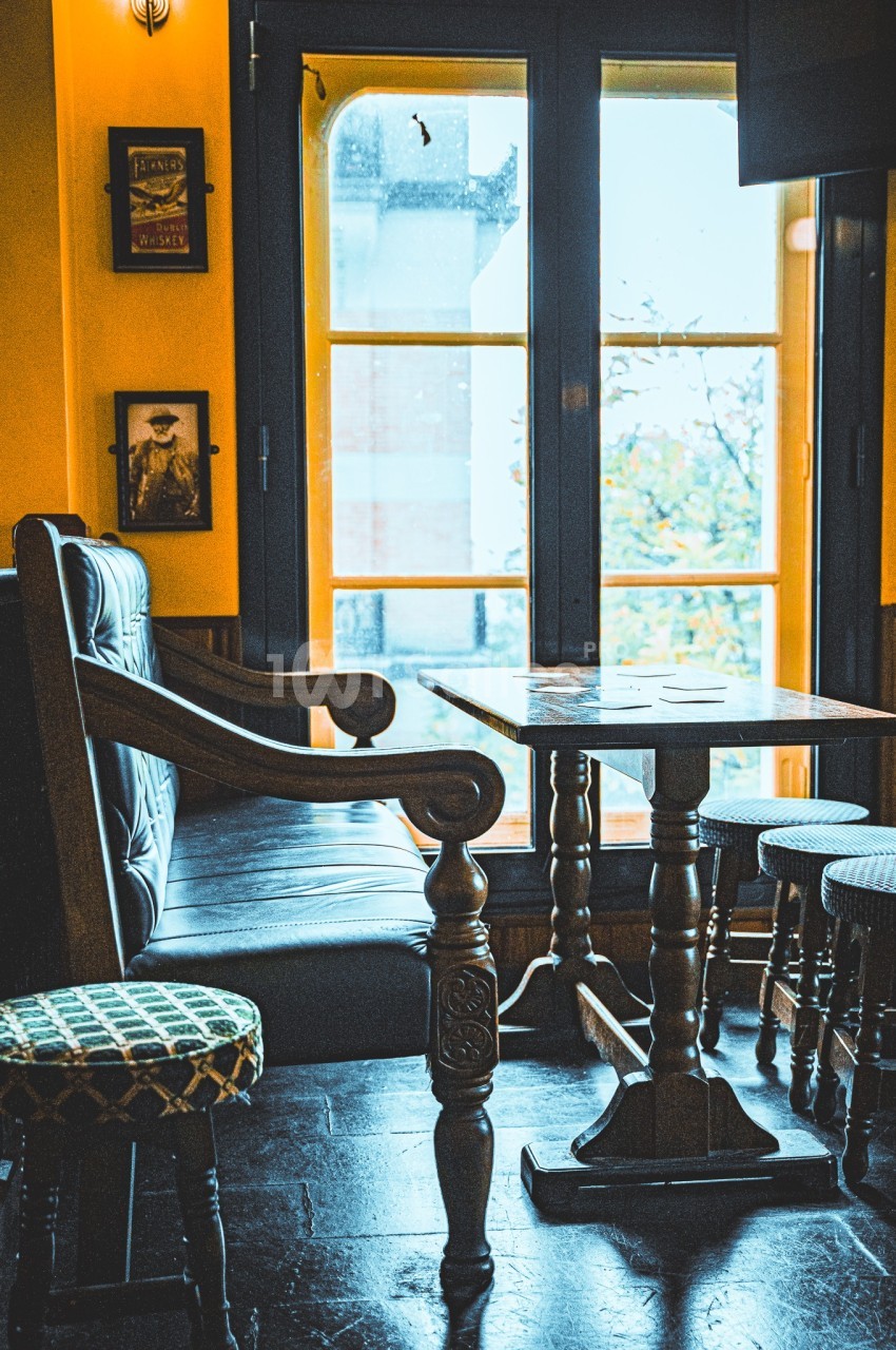 Intérieur d'un café avec une table en bois, des chaises et un banc près d'une fenêtre laissant entrer la lumière.