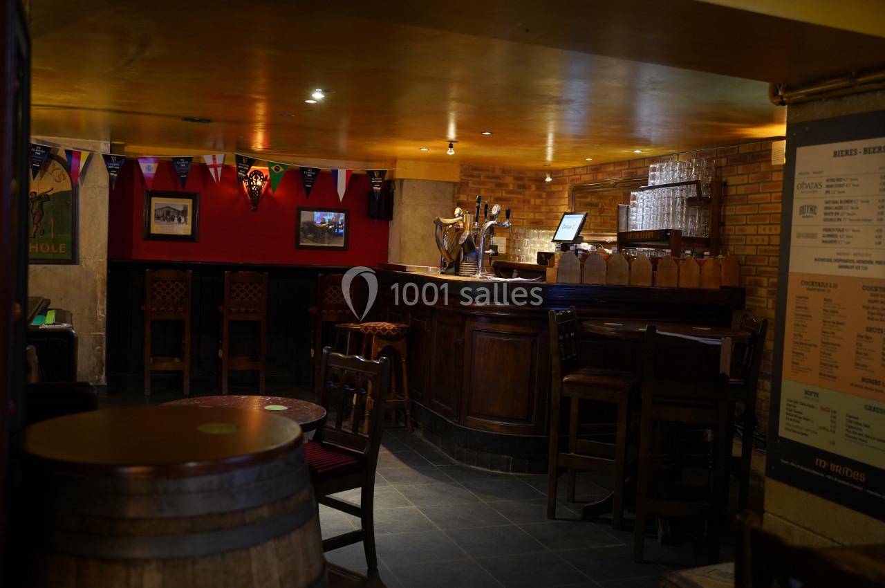 Intérieur d'un pub avec un comptoir en bois, des tabourets hauts, des décorations murales et un éclairage tamisé.