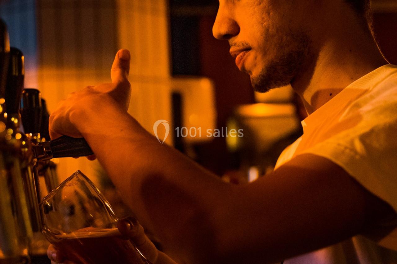 Un barman sert une bière pression dans un verre, éclairé par une lumière chaude dans un bar.