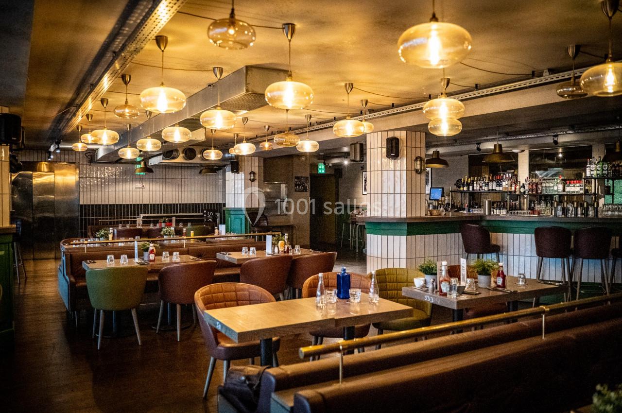 Salle de restaurant moderne avec tables en bois, chaises colorées et éclairage suspendu chaleureux.