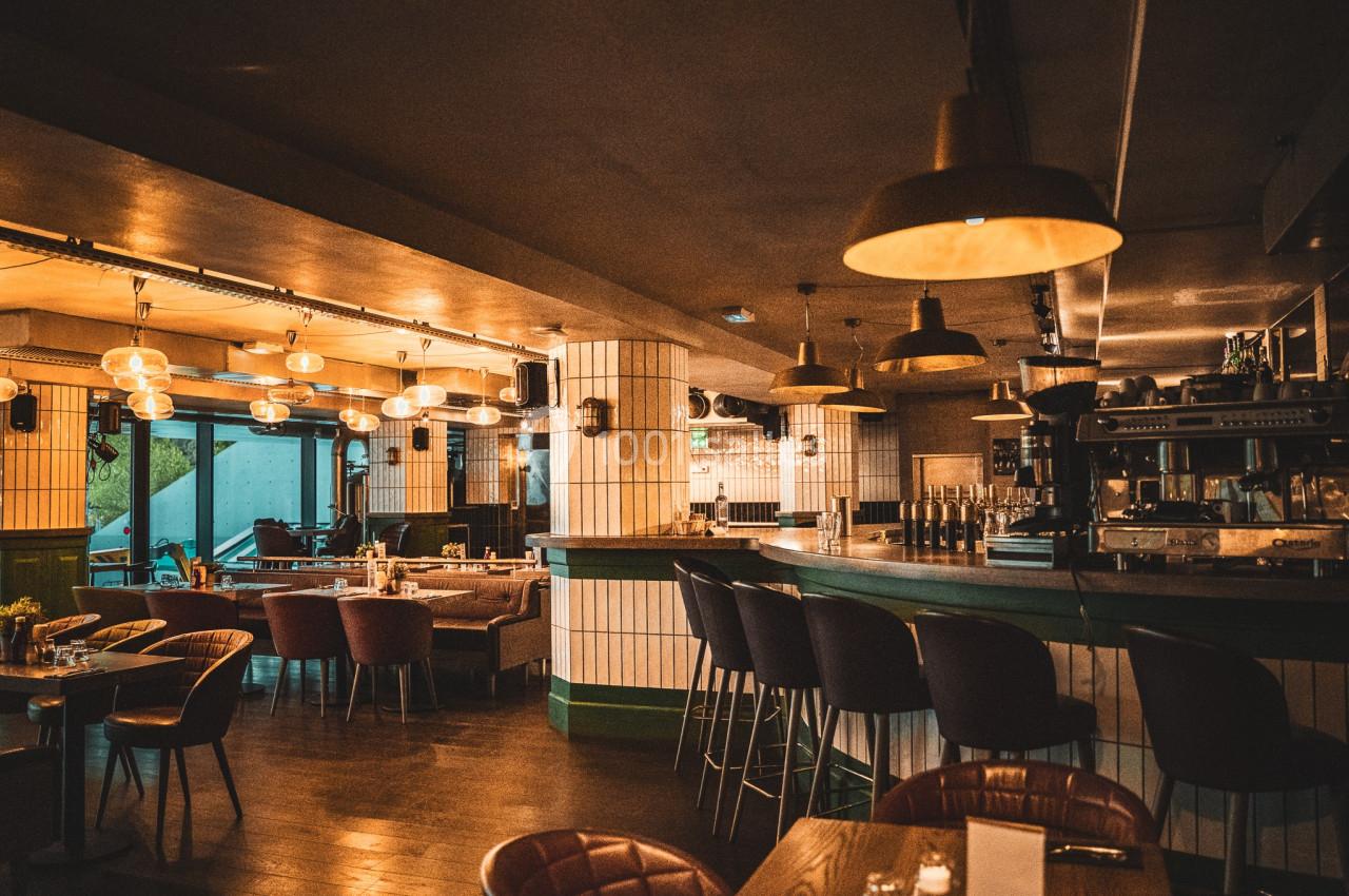 Intérieur d'un bar-restaurant avec comptoir, tabourets, tables, chaises et éclairage chaleureux.