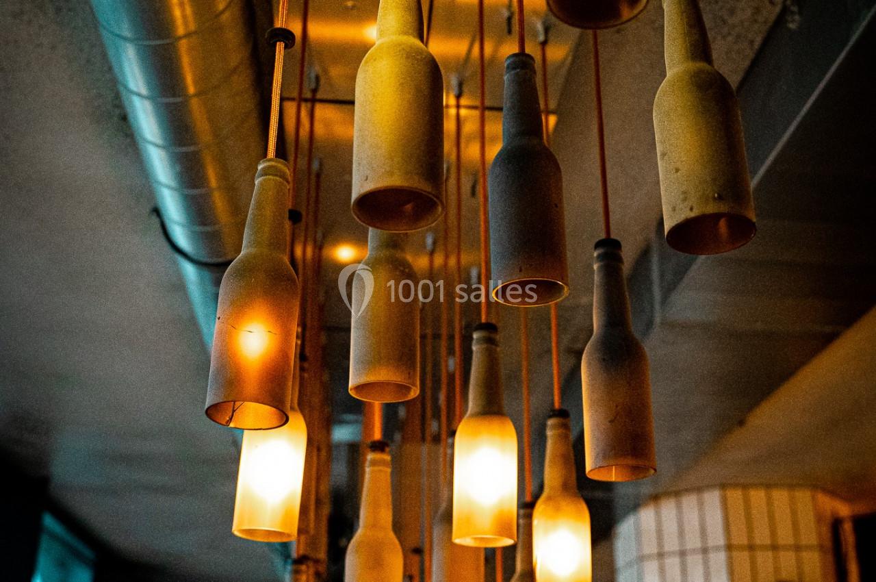 Suspension lumineuse composée de bouteilles recyclées éclairées, accrochées au plafond dans un intérieur moderne.