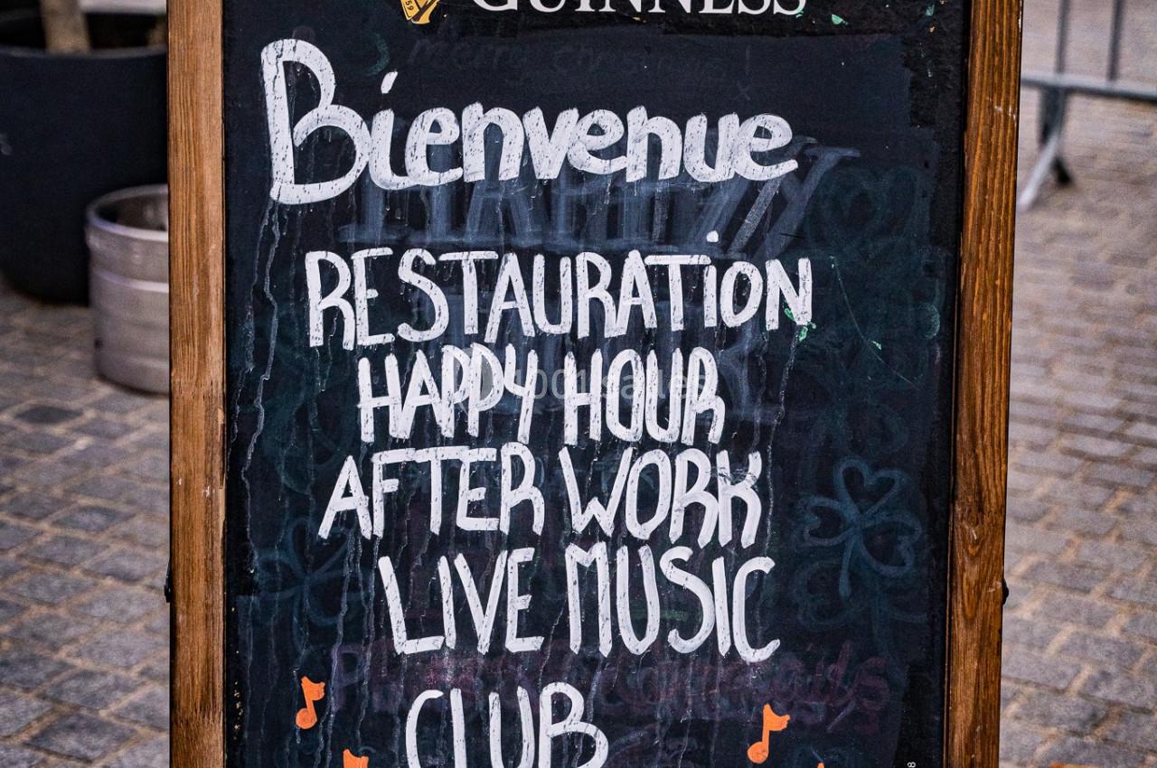 Tableau noir devant un établissement annonçant restauration, happy hour, musique live et club.