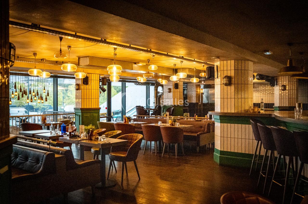Salle de restaurant chaleureuse avec mobilier en bois et cuir, éclairage suspendu et grandes baies vitrées.