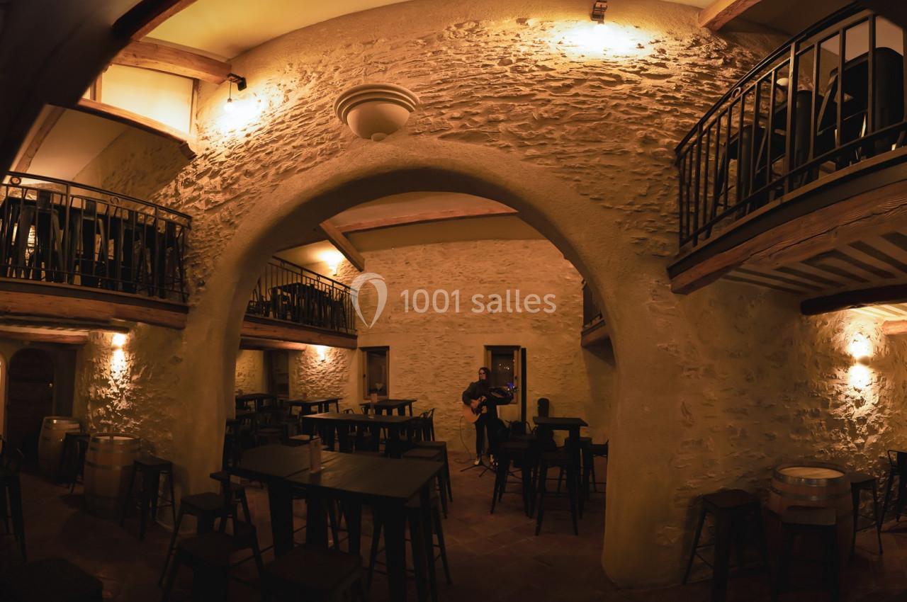 Location salle Aix-en-Provence (Bouches-du-Rhône) - Maneo #10 Salle intérieure en pierre avec arches, éclairage chaleureux, tables et chaises en bois, mezzanine avec balustrades.