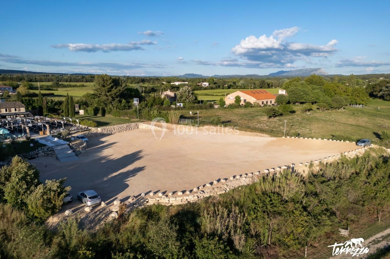 Location salle Aix-en-Provence (Bouches-du-Rhône) - Maneo #4 Vue aérienne d'un grand parking en gravier entouré de verdure, avec des bâtiments et des collines à l'arrière-plan.