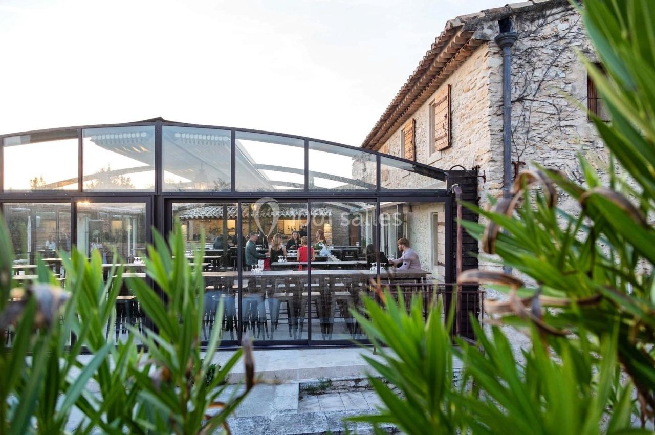 Location salle Aix-en-Provence (Bouches-du-Rhône) - Maneo #14 Salle de restaurant lumineuse avec verrière, tables dressées et clients attablés, entourée de végétation.