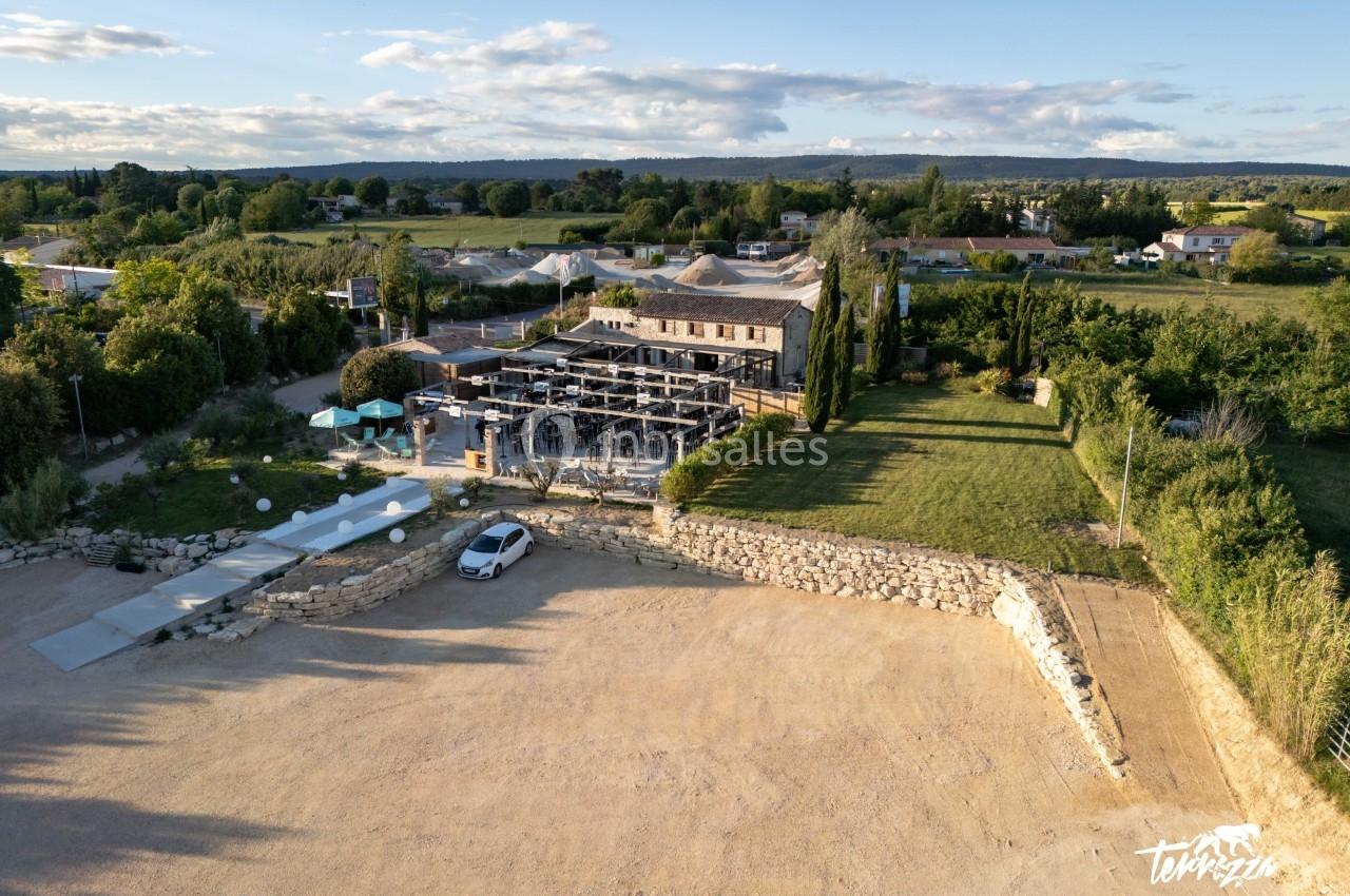 Location salle Aix-en-Provence (Bouches-du-Rhône) - Maneo #3 Vue aérienne d'un bâtiment en pierre avec une terrasse aménagée, entouré de verdure et d'un parking en gravier.
