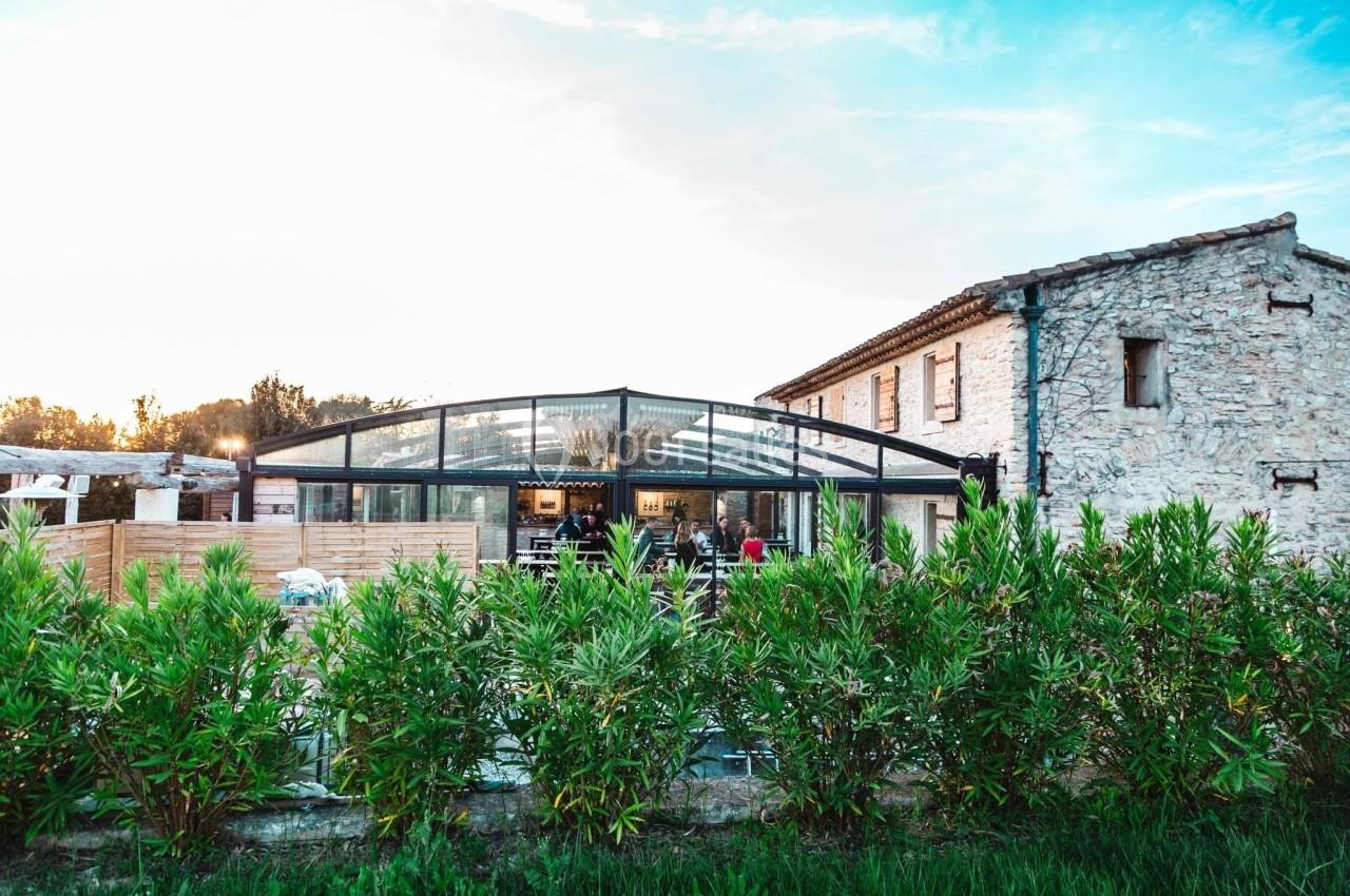 Location salle Aix-en-Provence (Bouches-du-Rhône) - Maneo #15 Bâtiment en pierre avec une verrière moderne entourée de végétation sous un ciel dégagé.
