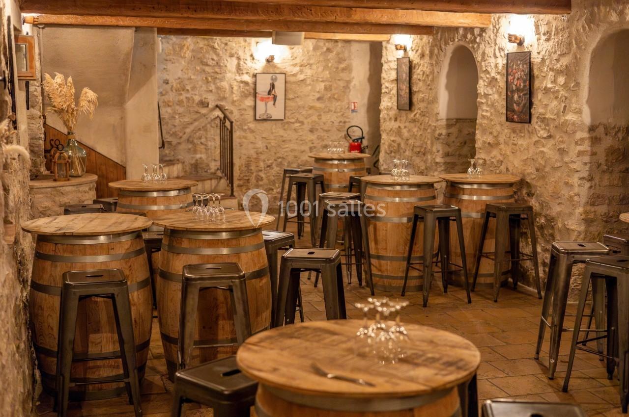 Location salle Aix-en-Provence (Bouches-du-Rhône) - Maneo #19 Salle rustique avec murs en pierre, tonneaux en bois servant de tables, tabourets métalliques et éclairage chaleureux.