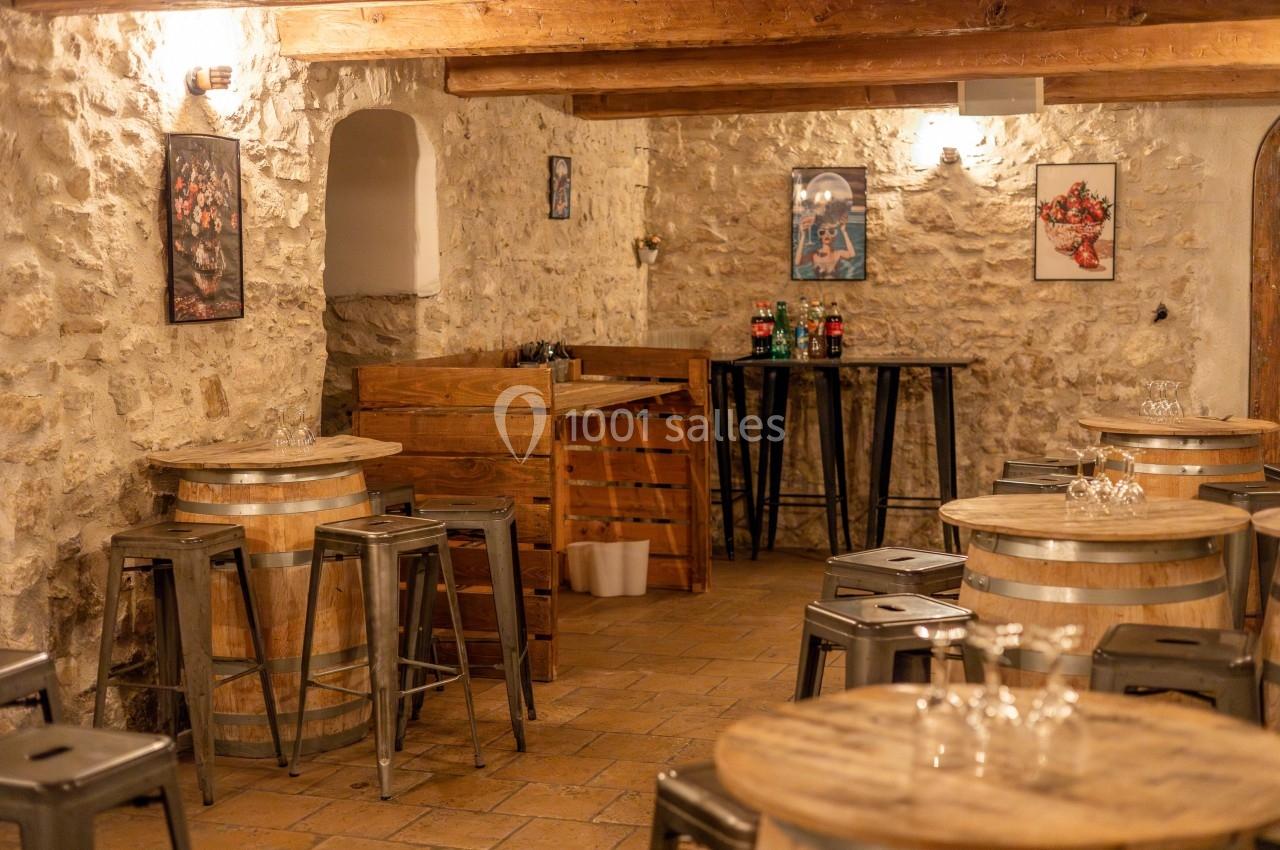 Location salle Aix-en-Provence (Bouches-du-Rhône) - Maneo #20 Salle rustique avec murs en pierre, tonneaux en bois servant de tables, tabourets métalliques et éclairage chaleureux.