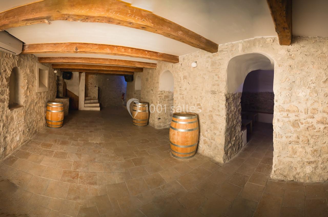 Salle voûtée en pierre avec des tonneaux en bois, un sol carrelé et des poutres apparentes au plafond.