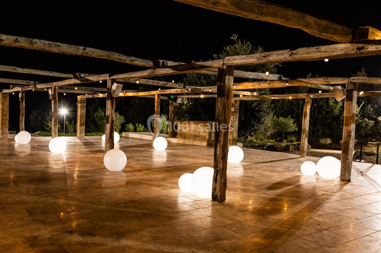 Structure en bois éclairée la nuit, avec des sphères lumineuses blanches posées sur un sol en pierre.