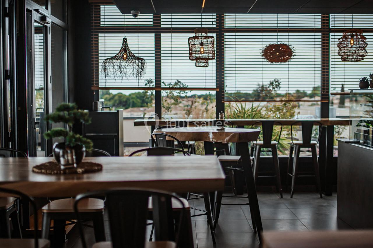 Salle de restaurant moderne avec tables en bois, chaises noires et grandes fenêtres donnant sur un paysage extérieur.