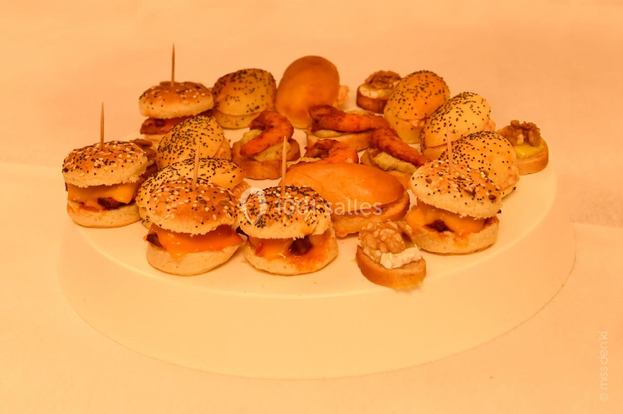 Assortiment de mini-burgers, bouchées apéritives et amuse-bouches disposés sur un plateau rond blanc.