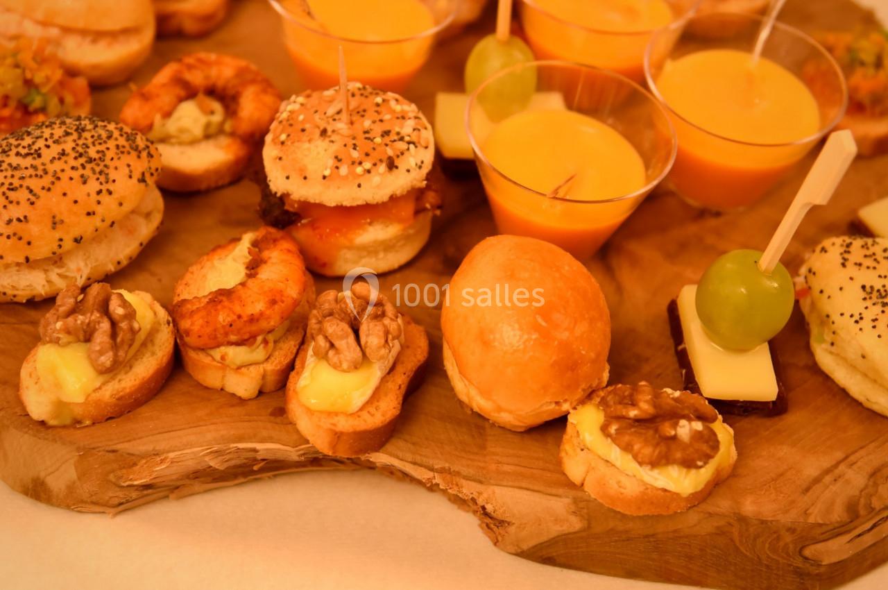 Plateau en bois garni de mini-burgers, verrines de soupe orange et amuse-bouches variés, dont des noix et raisins.