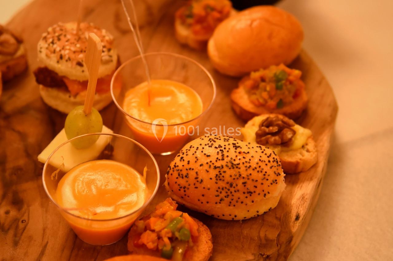 Plateau en bois avec des amuse-bouches variés, incluant verrines, pains garnis et bouchées salées, sur une table éclairée.