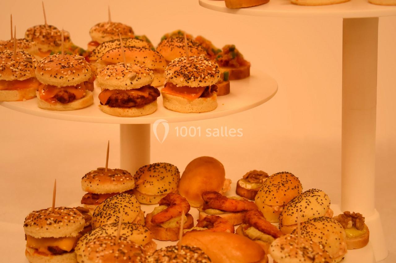 Plateaux de mini-burgers variés et amuse-bouches disposés sur des présentoirs blancs.