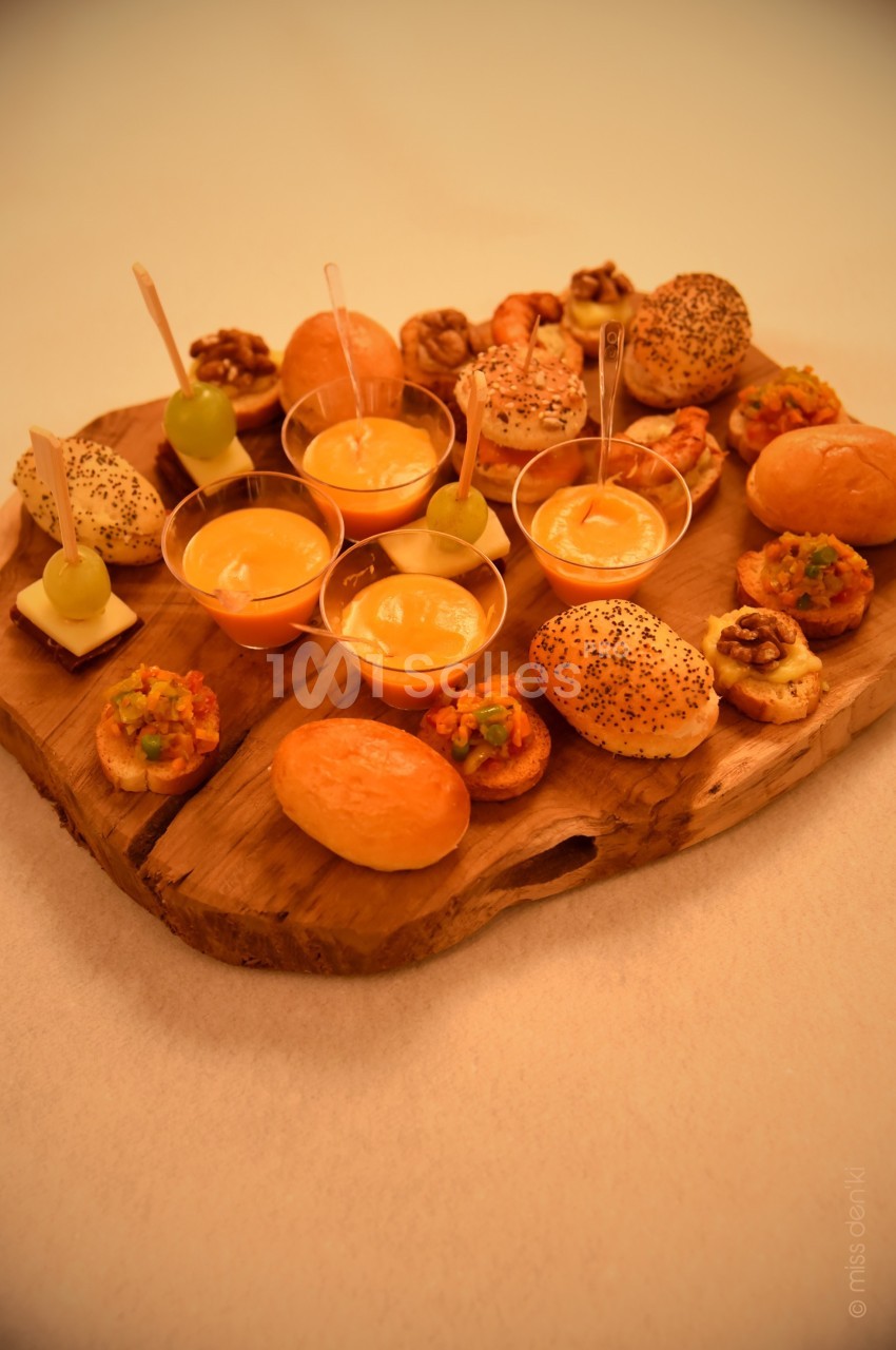 Plateau en bois garni de bouchées apéritives variées, incluant pains, verrines, fruits et noix.