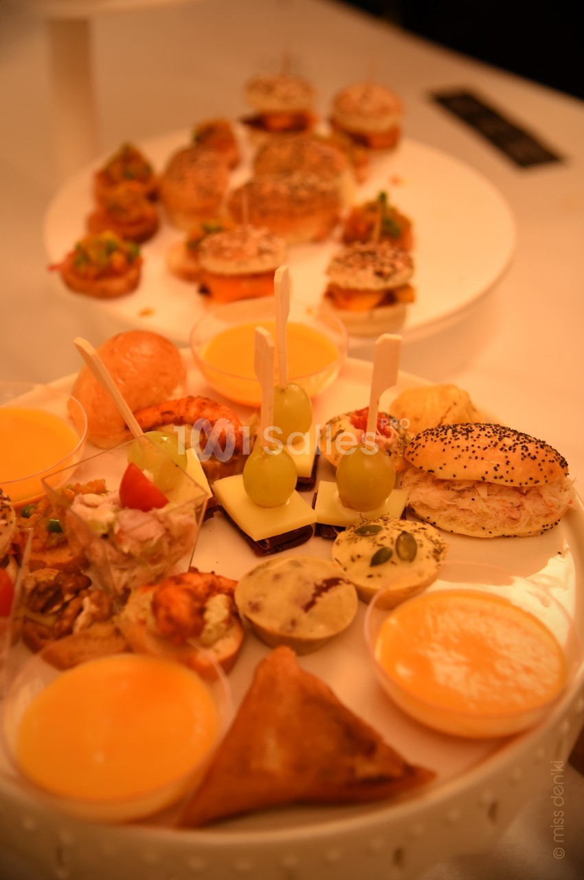 Plateaux de bouchées apéritives variées, incluant mini-sandwichs, verrines, brochettes et samoussas, disposés sur une table.