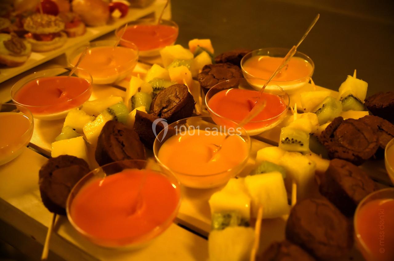 Assortiment de desserts comprenant brochettes de fruits, brownies et verrines colorées sur une table.