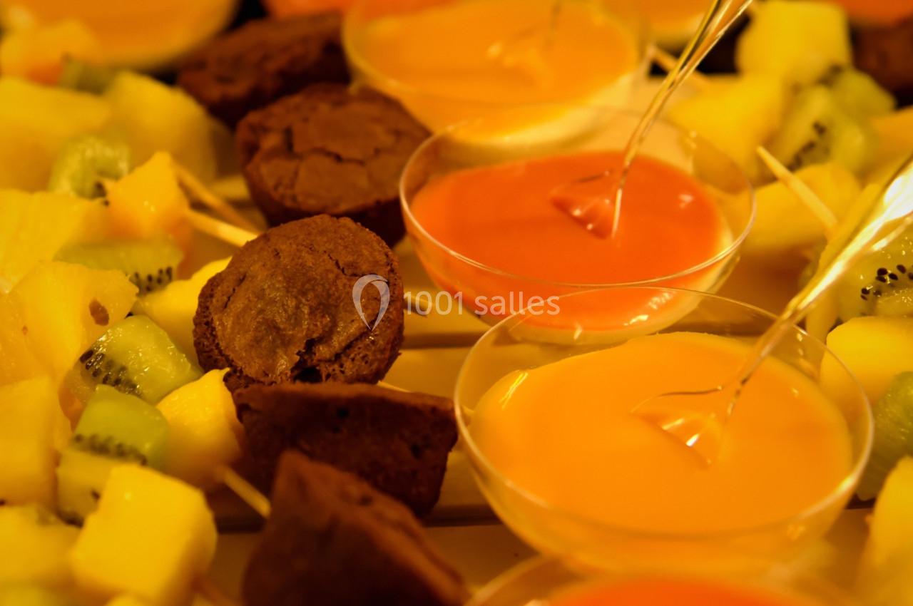Brochettes de fruits et morceaux de gâteau accompagnés de verrines de sauces colorées sur une table.